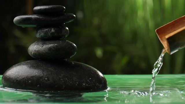 Water pouring from bamboo into lake with stack of zen stones in oriental garden