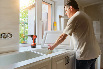 Middle-aged Caucasian man holds kitchen cabinet door , preparing for the process of custom installation in his own house. Quarantine activity, repair concept