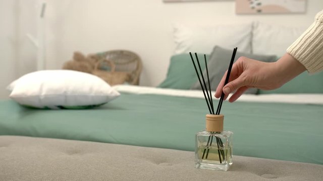 Woman putting air reed diffuser on bedside bench in room