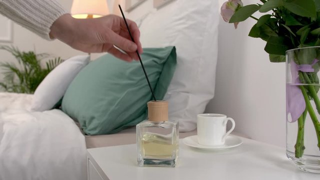 Woman putting air reed diffuser on bedside table in room