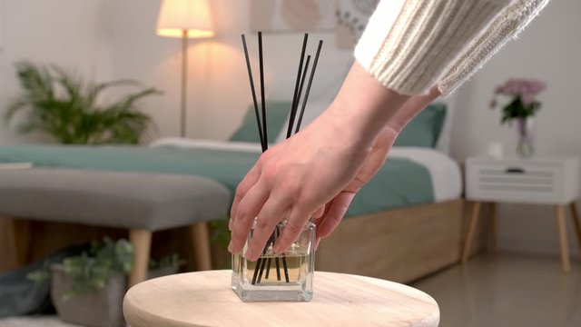 Woman putting air reed diffuser on table in bedroom