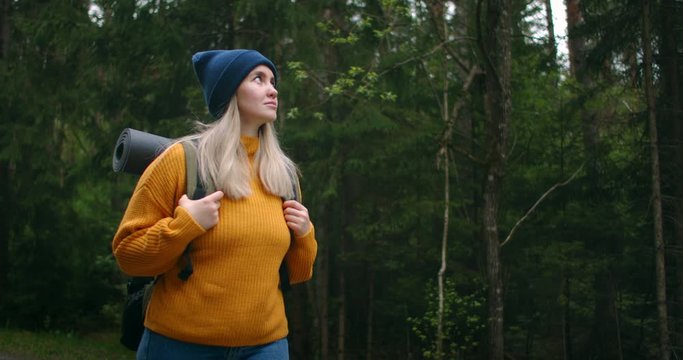 Slow motion female hiker walks along levada trail in forest. Happy female backpacker admiring nature walking on countryside road. Woman tourist walking in the fall forest on sunny autumn day.