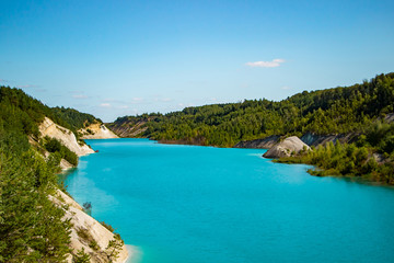 Fototapeta na wymiar Unusual lake with turquoise water in the crater. Rocky stony shore chalk quarry in Belarus.