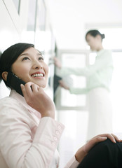 Obraz premium Businesswoman talking on the phone, colleague searching for files in the background