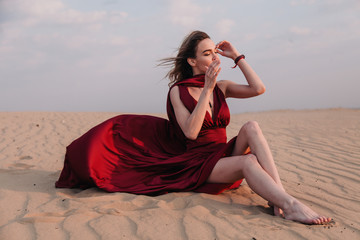 Fototapeta na wymiar The girl in the red dress sits in the wind in the desert