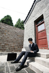 Businessman with telephone headset sitting on stairway using laptop