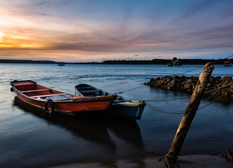 Fototapeta na wymiar Beautiful sunset on the edge of the lake. Two small boats tied to a pole.