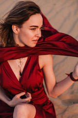 The girl in the red dress sits in the wind in the desert