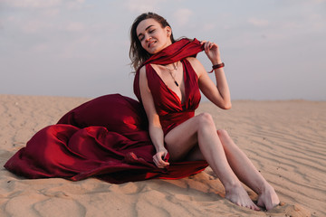 The girl in the red dress sits in the wind in the desert