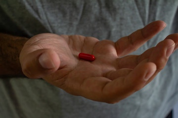 Hand of a man wearing a gray t-shirt holding a red capsule in his hand.