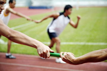 Man passing baton to his teammate in a relay event - obrazy, fototapety, plakaty