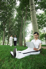 Woman using laptop, senior man and woman walking in the background