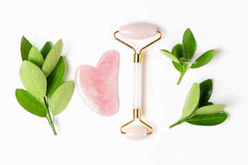 Facial roller and suache scraper with green leaves on white background, concept of facial massage