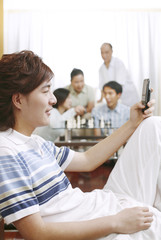 Obraz premium Man text messaging on the phone with people playing chess game in the background