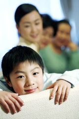 Boy lying on the couch smiling at the camera, the rest watching