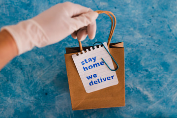 hand with glove holding takeaway shopping bags with Stay Home We Deliver message.