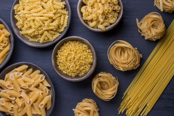 variety of noodles on black background in different containers - top