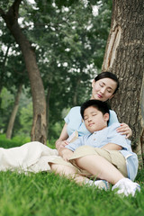 Fototapeta premium Woman and boy leaning against a tree with their eyes closed