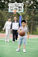 Obraz premium Boy dribbling basketball, senior man and woman watching