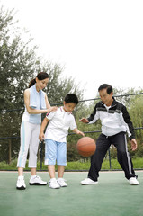 Fototapeta premium Boy dribbling basketball, woman and senior man watching