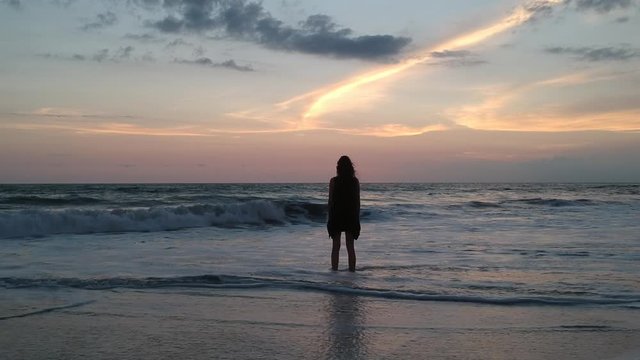 drone flies past a girl with her back to the frame in the ocean and catches up with the sunset and the sun asia...