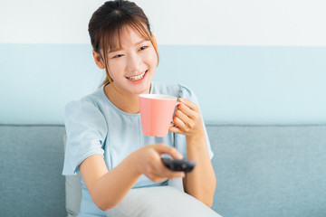 Young Asian woman sitting on sofa, drink coffee and watching television