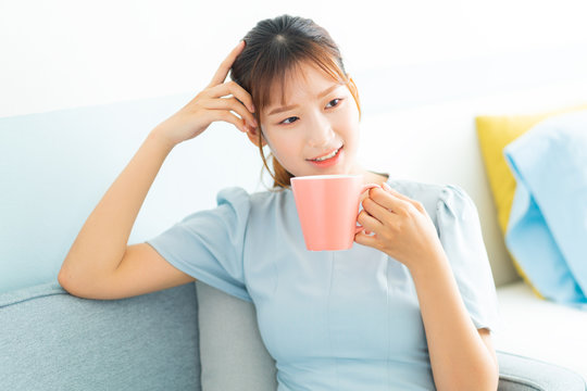Young Asian woman sitting on sofa, drink coffee and watching television