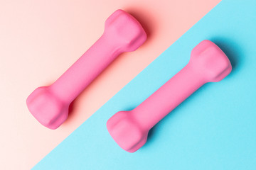 Pink dumbbells on a pink and blue background, a top view, sports background