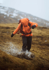 Woman in an orange windbreaker hiking under the rain at the Faroe Islands © rawpixel.com