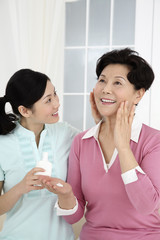 Woman helping senior woman to apply lotion