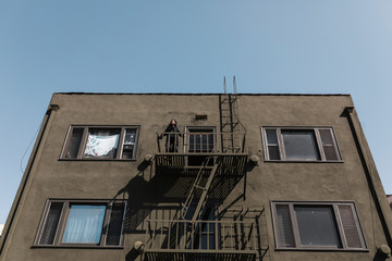 Woman standing at the fire escape of her apartment in downtown LA during the covid-19 pandemic.