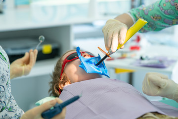 Dentist is treating a boy's teeth. Dentist examining boy's teeth in clinic. A small patient in the dental chair smiles. Dantist treats teeth