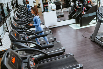 Fototapeta na wymiar A beautiful young caucasian girl is running in the gym on a treadmill