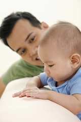 Baby standing on couch, man watching