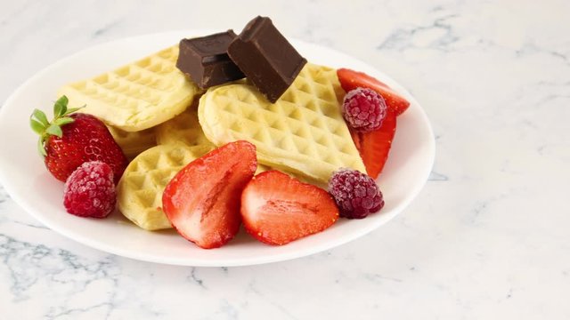 Waffles on white plate decorated with chocolate, strawberries and raspberries 