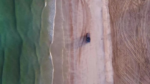 Aerial video trip of 4 wheel car driving along sandy beach washed by ocean waves.Footage of travelers having extreme vehicle adventure on seashore during summer journey, black car on an empty beach .