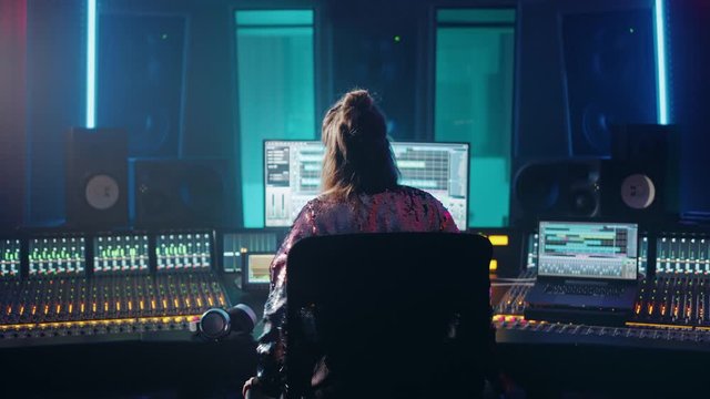 Stylish Artist, Musician, Audio Engineer, Producer Takes Place at His Control Desk in Music Record Studio, Uses Computer Screen show User Interface of DAW Software with Song Playing. Back View