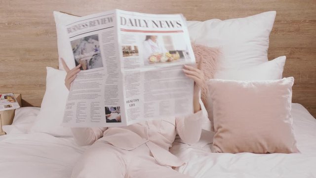 Morning of young woman with newspaper taking care of her skin at home