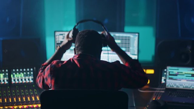 Stylish Artist, Musician, Audio Engineer, Producer Takes Place at His Control Desk in Music Record Studio, Uses Computer Screen show User Interface of DAW Software with Song Playing. Back View