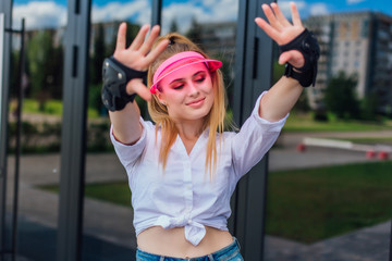 Portrait of an emotional girl in a pink cap visor and protective gloves for rollerblades and...