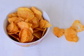 Close-up of potato chips or crisps in bowl against white background/ Unhealthy snack/ salty...