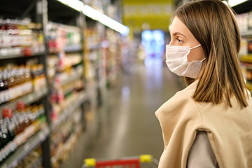 Close-up portrait of young woman wearing protective mask and buying food in grocery store during coronavirus pandemic. Covid-19. Copy space