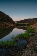 Fototapeta premium A lake in which the moon is reflected among the hills at dusk