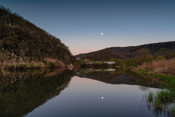 A lake in which the moon is reflected among the hills at dusk