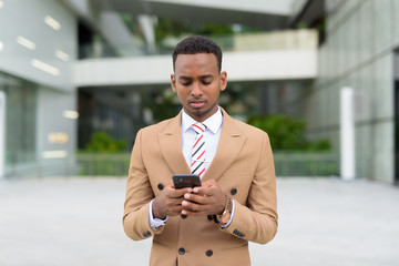 Young handsome African businessman using phone in the city outdoors