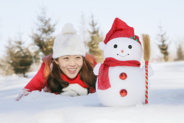 Woman in warm clothing lying on snow and looking at snowman