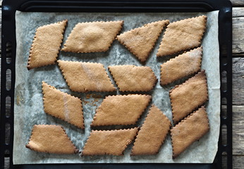 Background about natural dessert.Homemade diet cookies made from rye flour on parchment paper for baking on a black baking sheet on an ancient wooden table.