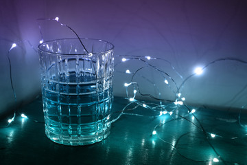 A whiskey glass with liquid in it, surrounded by magical Christmas fairy lights and a gradient glow