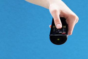 Fototapeta premium Close up of female hands holding a black remote control to switch channels on the TV on a blue background