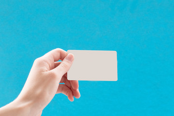 Close up of a female hand holding a blank white business card on a blue background. Business idea, copy space